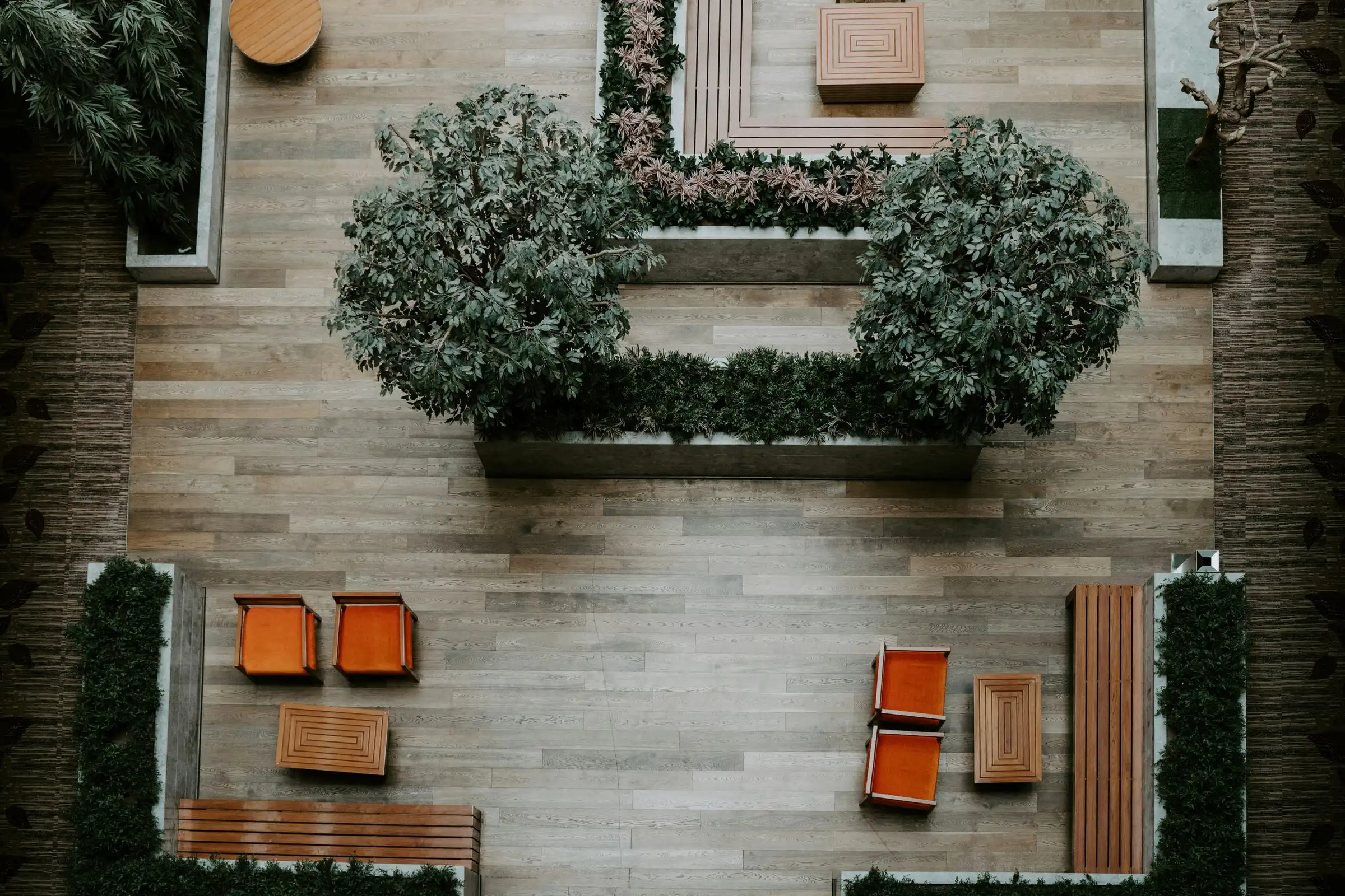 A courtyard from directly above: timber-look paving, clipped shrubs in planters and orange outdoor chairs