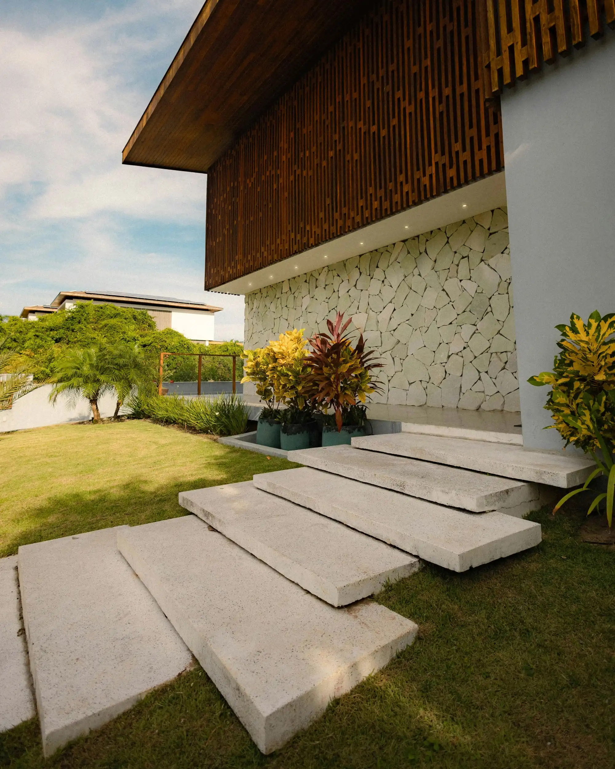 Wide concrete steps floating over a lawn beside a stone-clad wall, with bright planting at its foot
