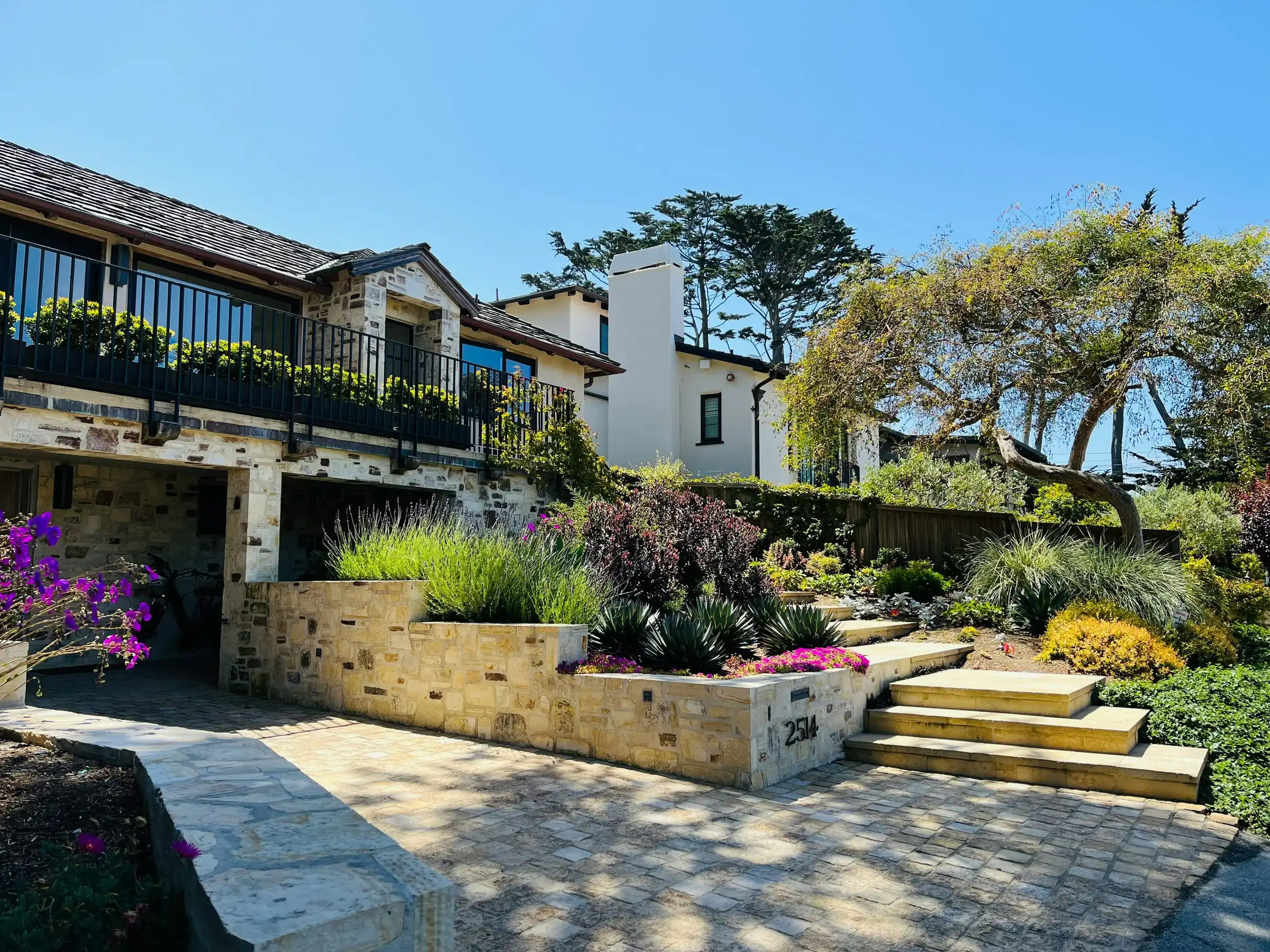 A sandstone block retaining wall in front of a house, planted along the top, with wide sandstone steps