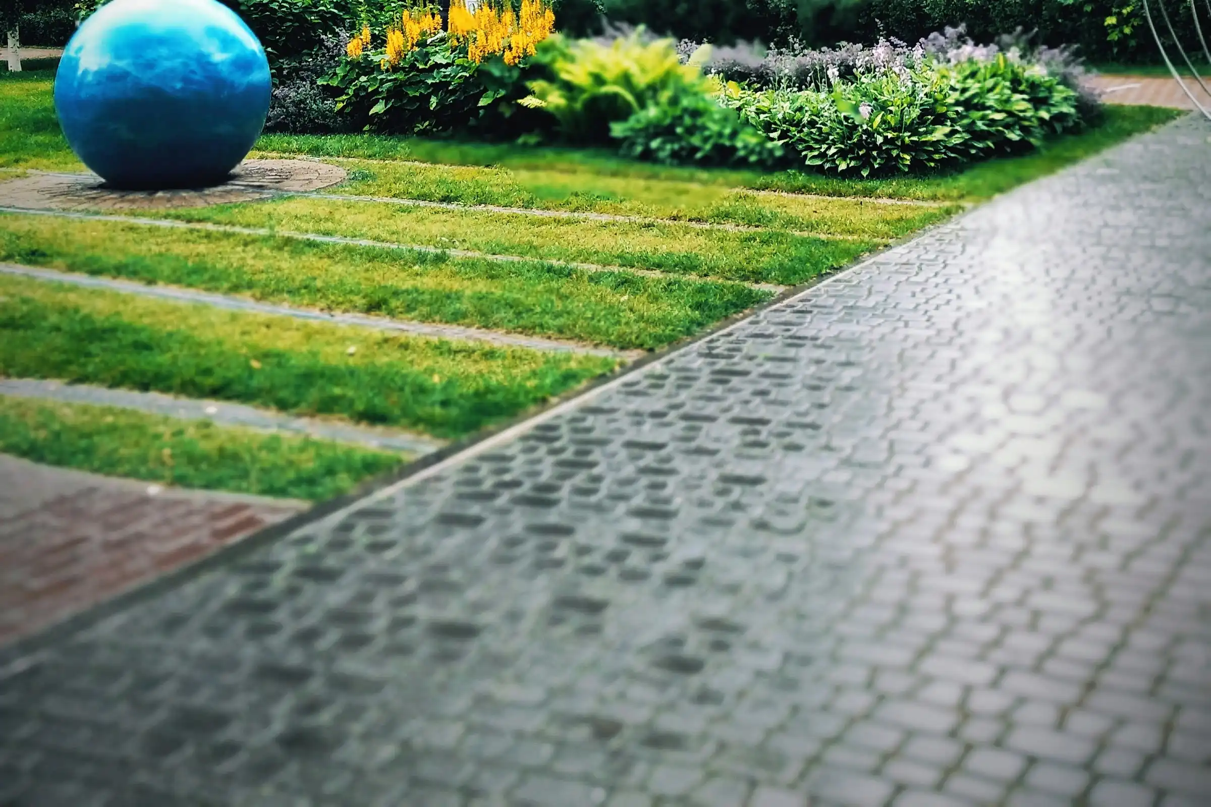 Fresh lawn laid in strips beside a dark cobbled path, with a garden bed beyond